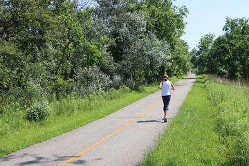Woman running alone on the North Branch Trail in summer at Watersmeet Woods in Glenview, Illinois