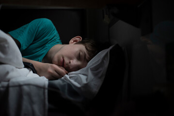 teenage boy sleeping on bottom bunk in train at night in darkness