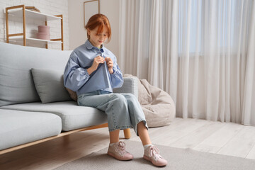 Teenage girl buttoning up shirt on sofa at home
