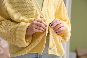 Teenage girl buttoning up yellow cardigan at home, closeup
