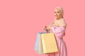 Fototapeta premium Beautiful Muslim woman in hijab with shopping bags on pink background