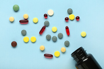 Black bottle with scattered pills on blue background, closeup