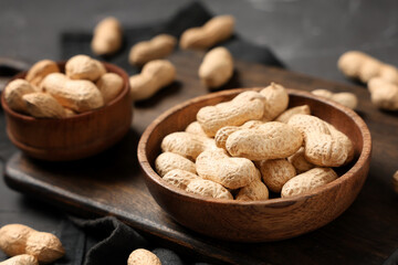 Wooden bowls with unpeeled peanuts on black background, closeup