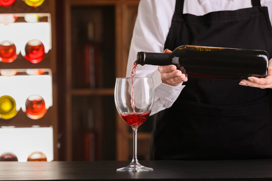 Bartender pouring of red wine from bottle into glass on bar counter in pub - Powered by Adobe