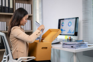 Businesswoman putting files into cardboard box at office desk