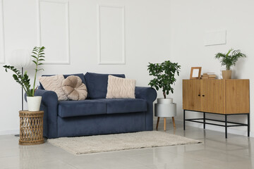 Obraz premium Cozy blue sofa with dresser, coffee table and houseplants near white wall in living room