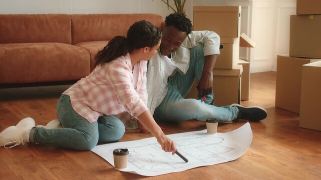 A couple reviews their new apartment plans on the floor surrounded by moving boxes. They seem excited about decorating and settling into their new space after relocating. - Powered by Adobe