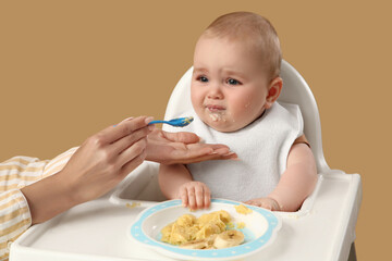 Mother feeding her little baby in high chair against beige background