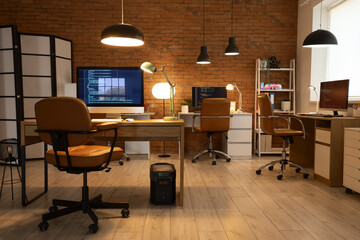 Interior of programmer's office with desks and glowing lamps in evening