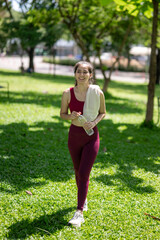 A woman is walking in a park with a bottle of water and a towel