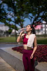 A woman is drinking water while wearing a red tank top and white towel
