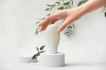Plaster podiums with bottle of cream, female hand and eucalyptus on white grunge background