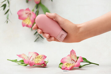 Female hand with bottle of cream, eucalyptus and alstroemeria flowers on white grunge background