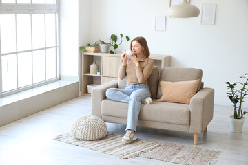 Young woman with cup of coffee sitting on grey couch in living room