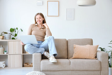 Young woman with laptop sitting on grey couch in living room