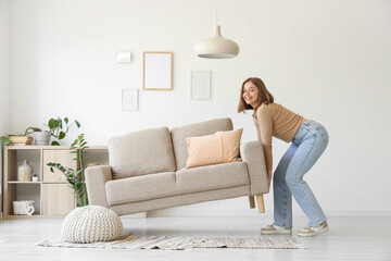 Young woman carrying grey couch in living room