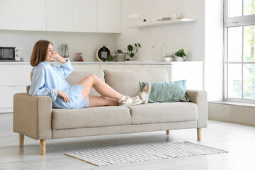 Young woman lying on grey couch in kitchen