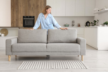 Young woman behind grey couch in kitchen