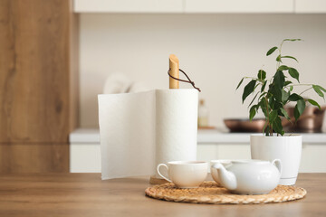 Roll of paper towels with cups of tea, teapot and houseplant on table in kitchen