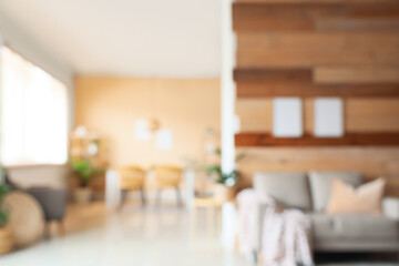 Blurred view of light living room with table, sofa and houseplant near wooden wall