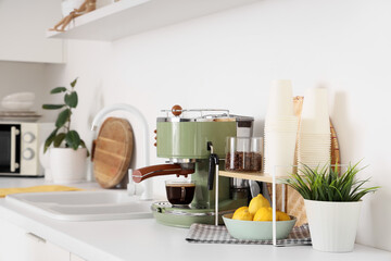 Modern coffee machine with cups, lemons and plants on counter in kitchen