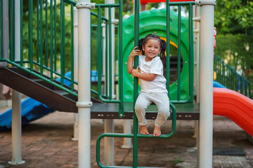 Obraz premium happy toddler girl playing and climbing on outdoor playground at park