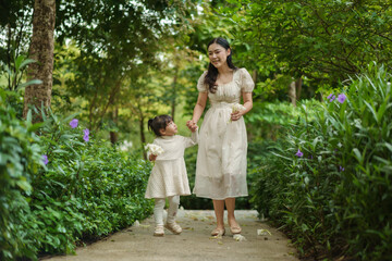 happy mother and toddler girl in white dress walking in flower garden