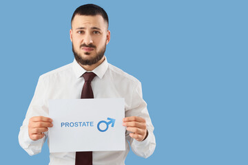 Young businessman holding paper with word PROSTATE on blue background. Cancer awareness concept