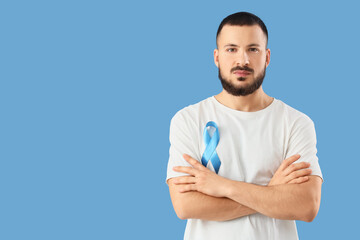 Young man with blue ribbon on color background. Prostate cancer awareness concept