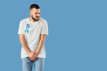 Young man with blue ribbon on color background. Prostate cancer awareness concept