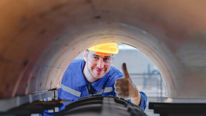 Smiling industrial engineer inspecting rotary die-cut mold from inside perspective, wearing protective gear and giving thumbs up during machine maintenance at corrugated box factory.