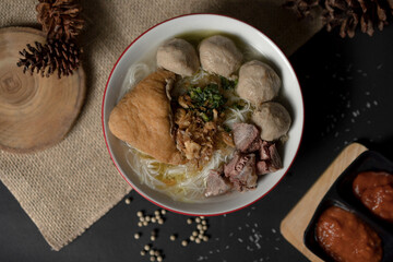 Top-down flat lay of a complete Bakso meal. Indonesian soup with beef, tofu, and meatballs on a decorated dark table with chili sauce.
