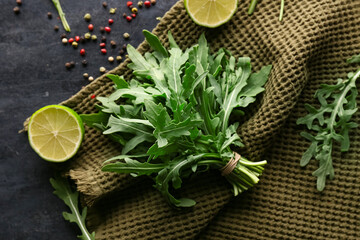 Bunch of fresh arugula leaves with lime and peppercorns on black background