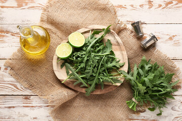 Plate with fresh arugula leaves and lime on white wooden background