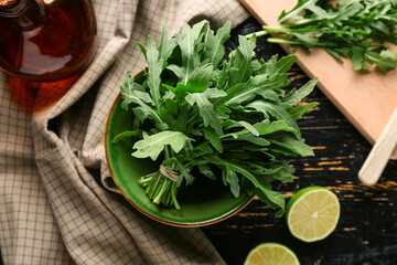 Bowl with bunch of fresh arugula leaves and lime on black wooden background