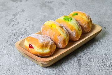 Close up view of four bomboloni doughnut with strawberry, pineapple and matcha filling on long wooden plate. homemade. Italian stuffed donuts. grey or gray cement on the background.