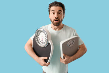 Shocked young man with weight scales on blue background