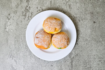 Top view of three bomboloni doughnut with strawberry, pineapple and matcha filling on white plate. homemade. Italian stuffed donuts. close up. grey or gray cement on the background. High angle. Above.