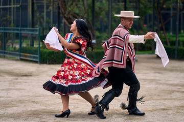 Portrait of a smiling young couple dressed as Chilean huasos,  joyfully dancing cueca outdoors....