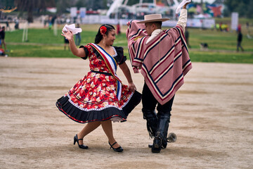 Portrait of a smiling young couple dressed as Chilean huasos,  joyfully dancing cueca outdoors....