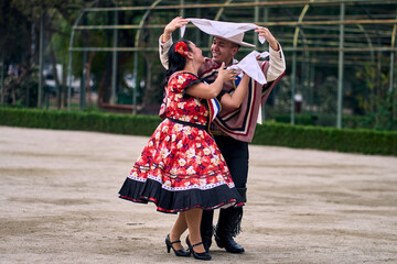 Portrait of a smiling young couple dressed as Chilean huasos,  joyfully dancing cueca outdoors....