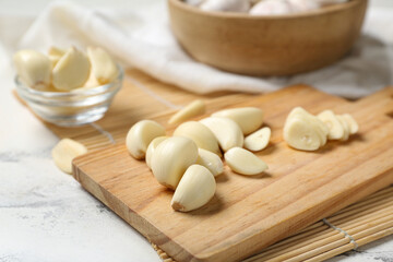 Wooden board and glass bowl with fresh garlic cloves on white background, closeup