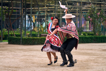 Portrait of a smiling young couple dressed as Chilean huasos,  joyfully dancing cueca outdoors. Traditional Chilean dance. Chilean traditions, celebrations.