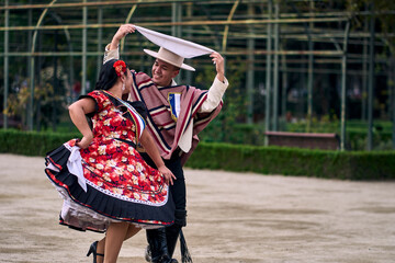 Portrait of a smiling young couple dressed as Chilean huasos,  joyfully dancing cueca outdoors. Traditional Chilean dance. Chilean traditions, celebrations.