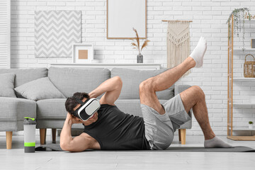 Sporty young man in VR glasses doing crunches at home