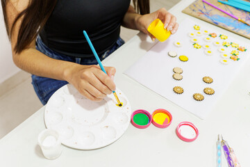 Female artist painting small wooden flower decorations with yellow acrylic paint using a paintbrush and palette