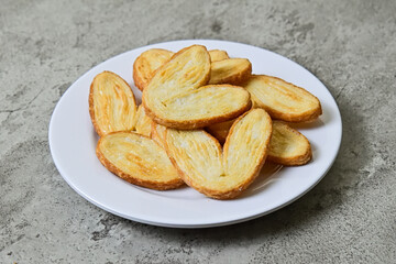 Close up view of many mini pies on white plate isolated on grey or gray cement background. Love sign. Danish. Pastry. Butter. Heart.