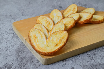Close up view of many mini pies on wooden cutting board isolated on grey or gray cement background. Love sign. Heart. Danish. Butter. Pastry.