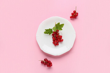 Plate with fresh red currants on pink background