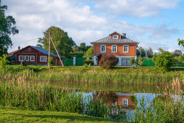 Russian traditional wooden houses decorated with wood carvings and a front garden on the banks of the Kamenka River on a sunny summer day, Suzdal, Vladimir region, Russia